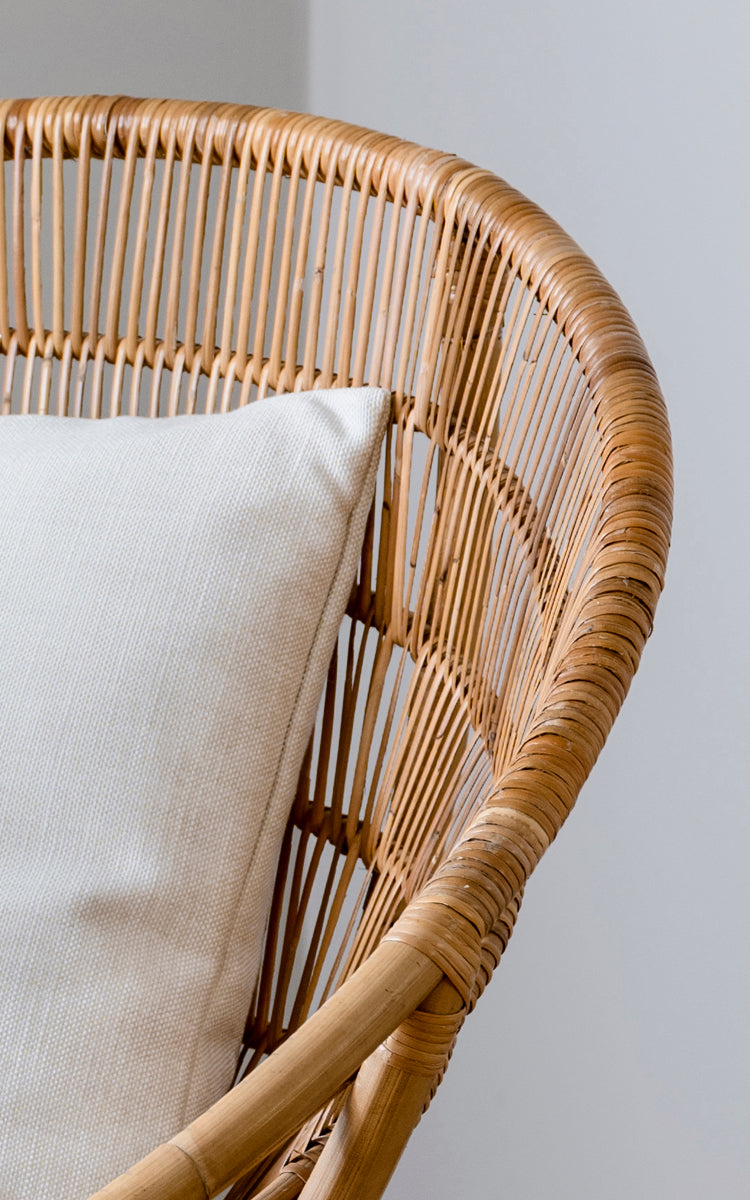 This is a close-up image of Luna Lounge Chair in natural skin on rattan. The curved frame with vertical slats and white cushion highlight the design.