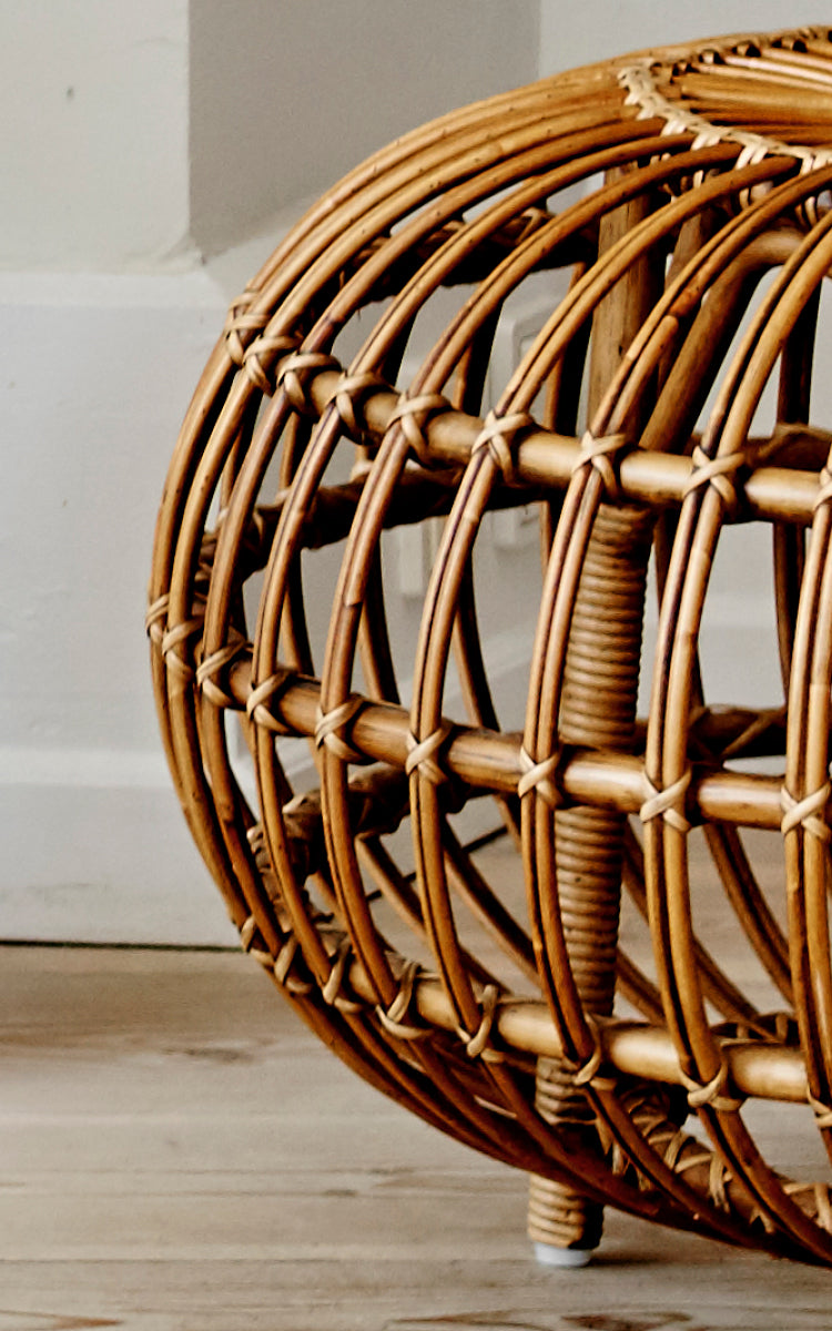 This is a close-up image of Ottoman Large in polished antique rattan. Detail of the large open rattan cage with curved ribs on wood floor.