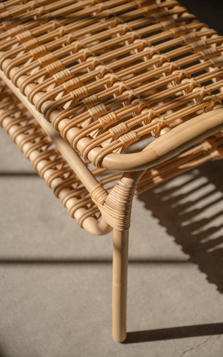 This is a close-up image of Machiya Bench in polished natural rattan. Slatted seat and shelf with sharp window shadows.