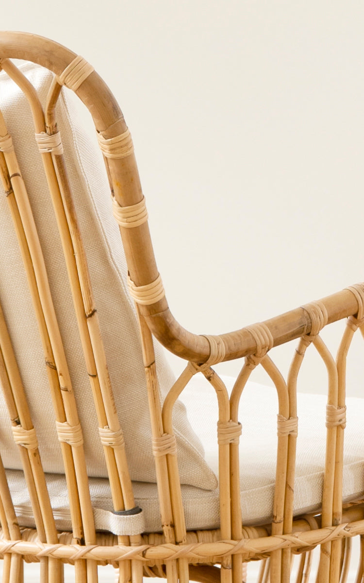 This is a close-up image of Tulip Lounge Chair in polished natural rattan. Detail of the rattan frame, arched braces and linen cushion.