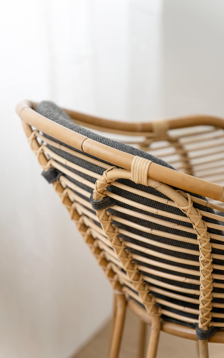This is a close-up image of Swing Lounge Chair in polished natural rattan. Detail of the curved rattan top rail and plaited back-rest binding.