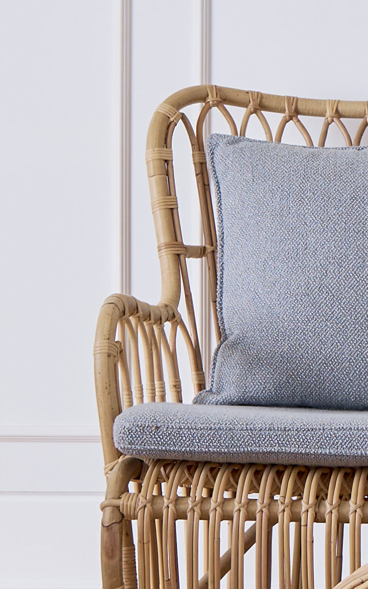 This is a close-up image of Tulip Sofa in polished natural rattan. Detail of the rattan sofa frame with arched braces and bouclé cushion.