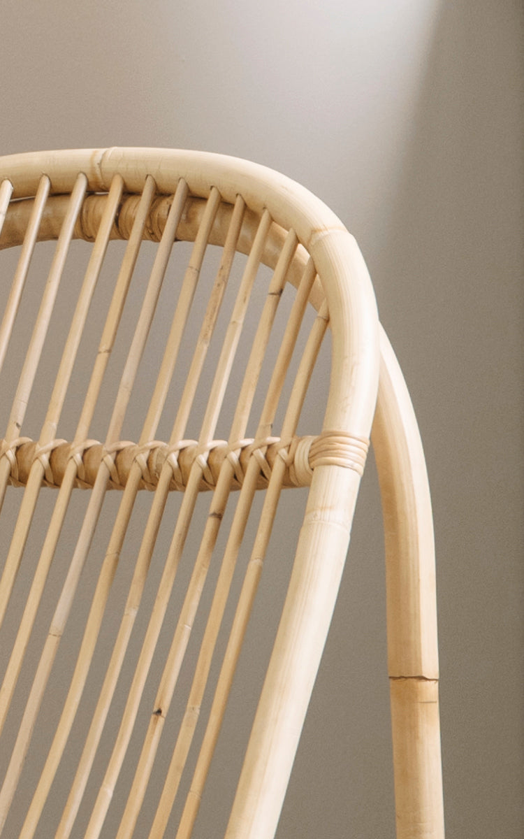 This is a close-up image of Nanny Rocking Chair in polished natural rattan. Detail of the smooth bent rods and circular rocker base.