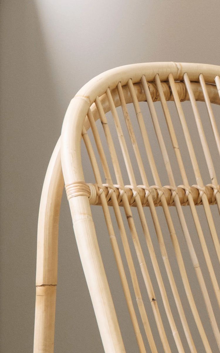 This is a close-up image of Nanny Rocking Chair in polished natural rattan. Detail of the smooth bent rods and circular rocker base.