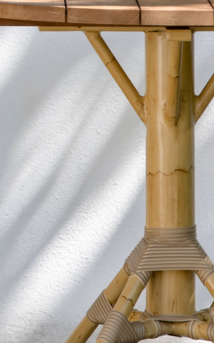 This is a close-up image of Nicole Cáfe Table | Teak Ø80 cm in natural aluminium artfibre. Detail of the woven texture and frame construction.