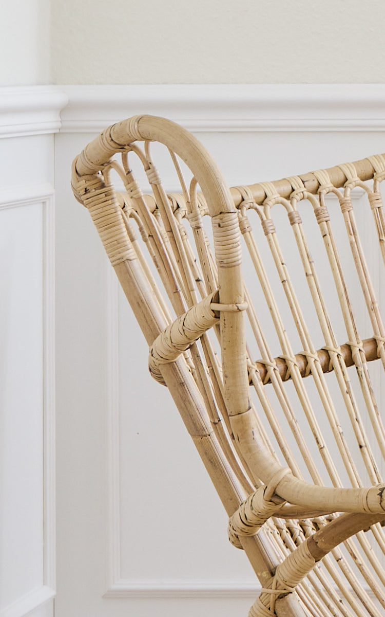 This is a close-up image of Teddy Lounge Chair in polished natural rattan. Detail of the curved rattan top rail and spindle back.