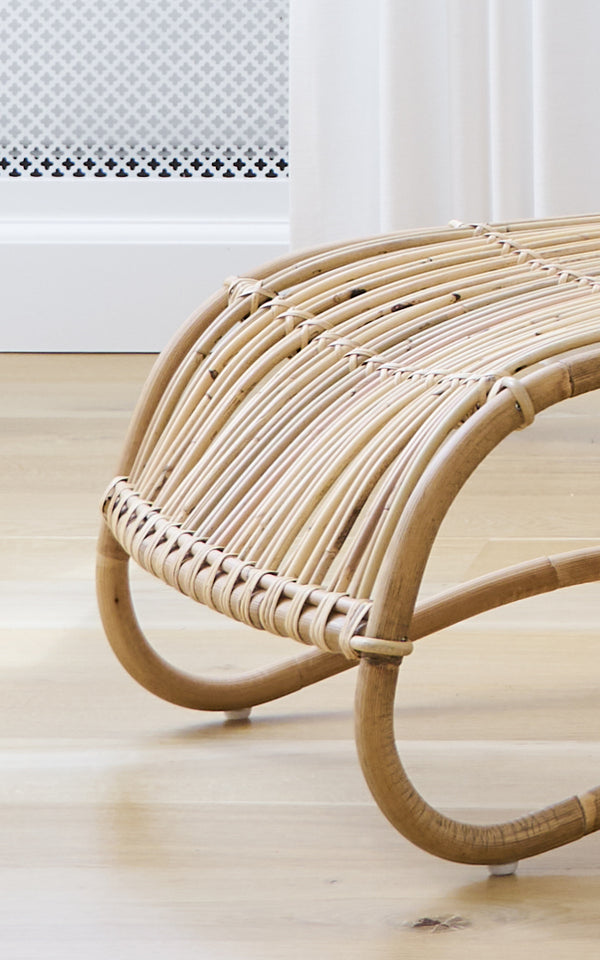 This is a close-up image of Teddy Footstool in polished natural rattan. Detail of the curved rattan rails and plaited wrap of the footstool.