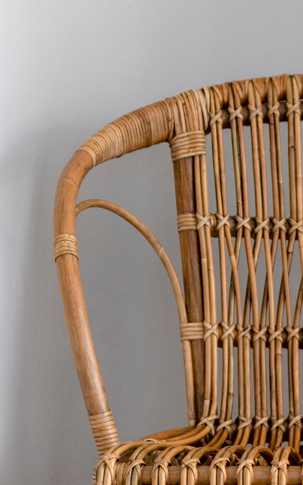 This is a close-up image of Robert Dining Chair in polished antique rattan. Detail of the curved rattan arm and spindle back with wrapped joints.