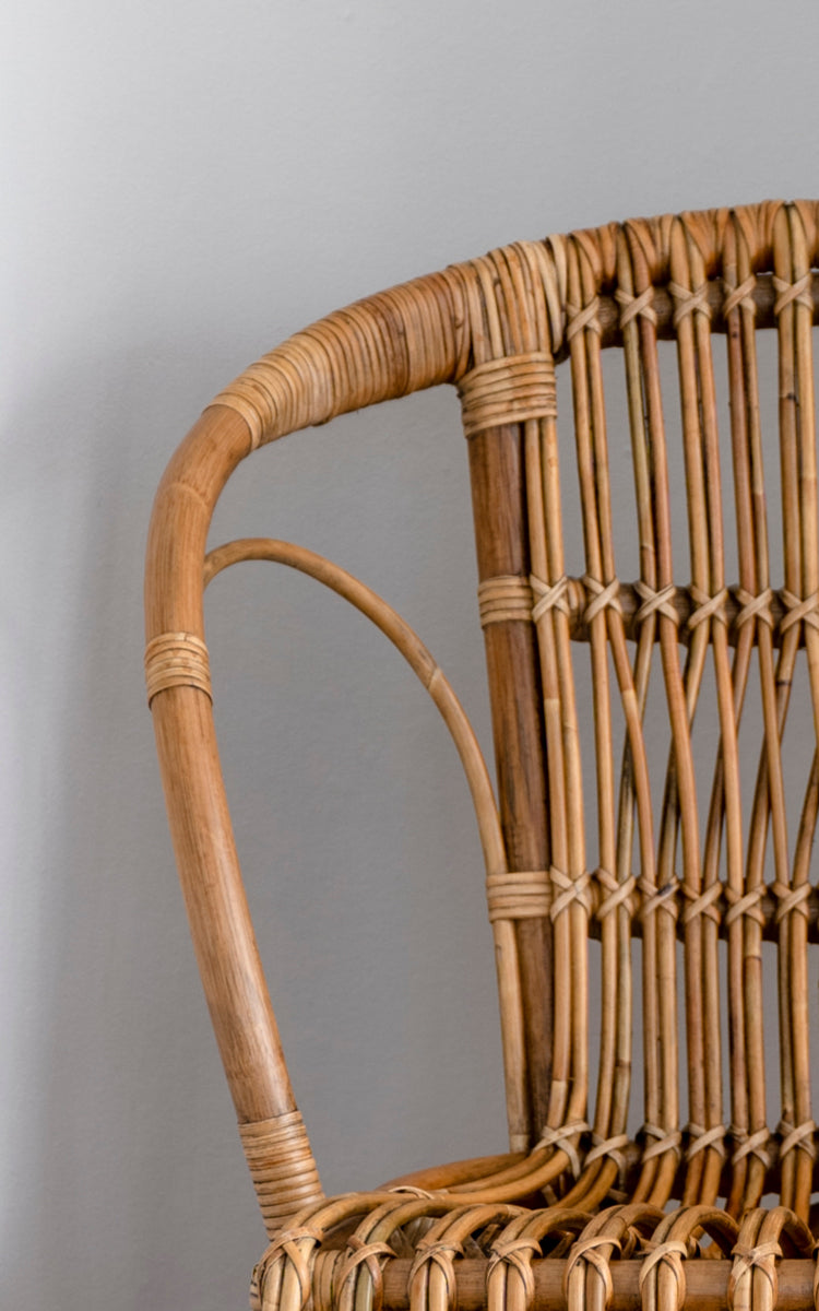 This is a close-up image of Robert Dining Chair in polished antique rattan. Detail of the curved rattan arm and spindle back with wrapped joints.
