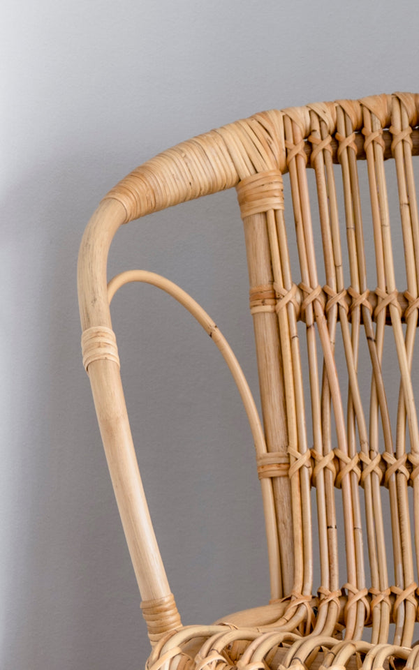 This is a close-up image of Robert Dining Chair in polished natural rattan. Detail of the natural curved rattan arm and spindle back.