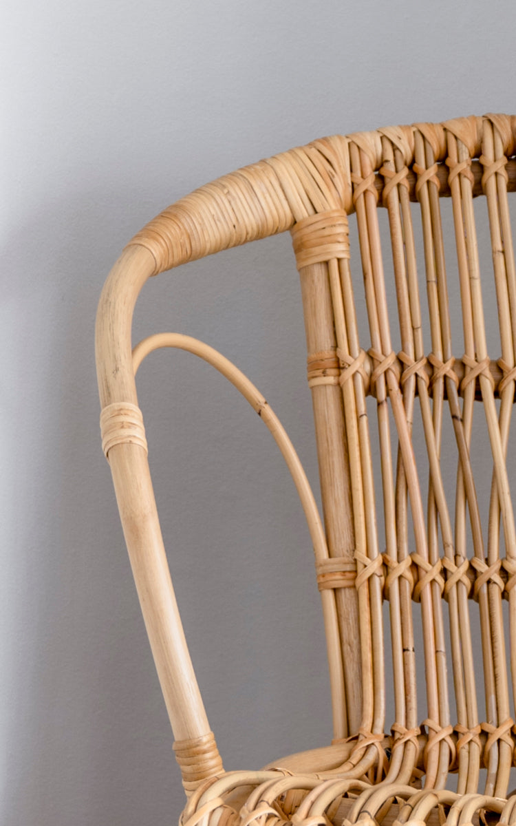 This is a close-up image of Robert Dining Chair in polished natural rattan. Detail of the natural curved rattan arm and spindle back.