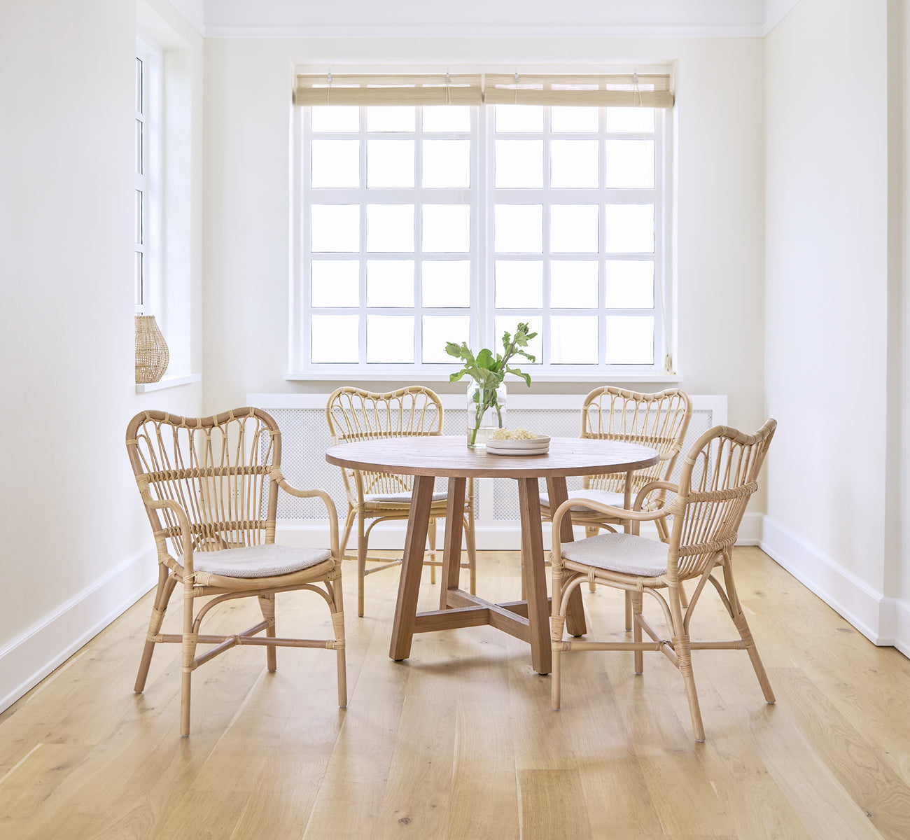 This is a lifestyle image of Margret Dining Chair in natural rattan. Bright white room with round dining table and oak floor.