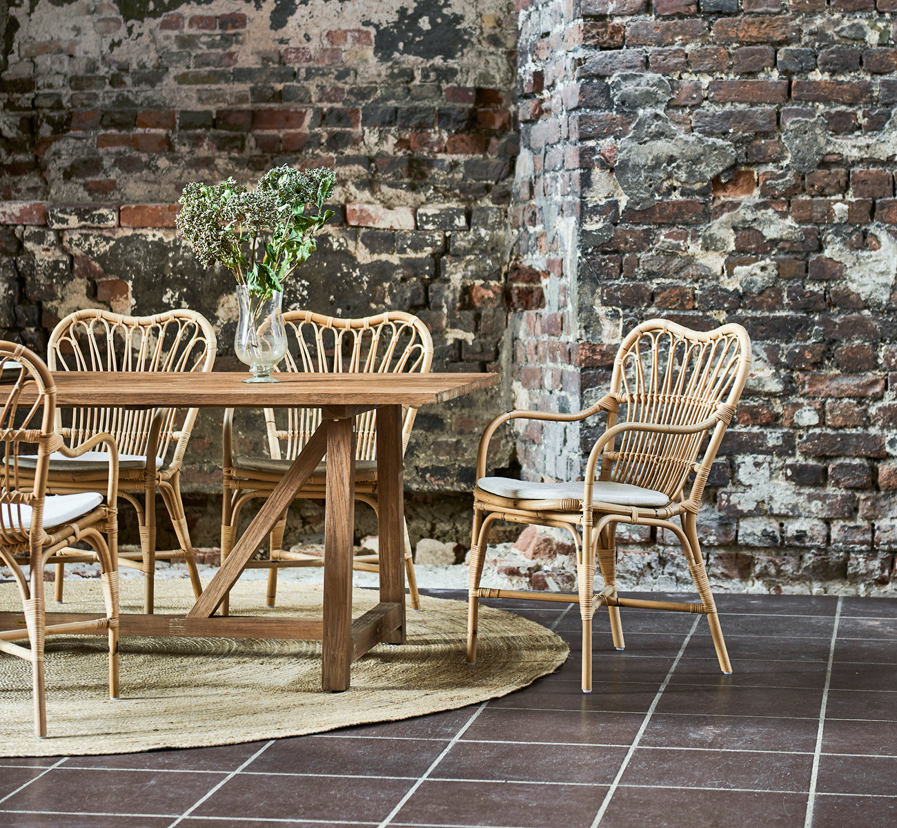 This is a lifestyle image of Margret Dining Chair in natural rattan. Industrial loft with exposed brick wall and jute rug.