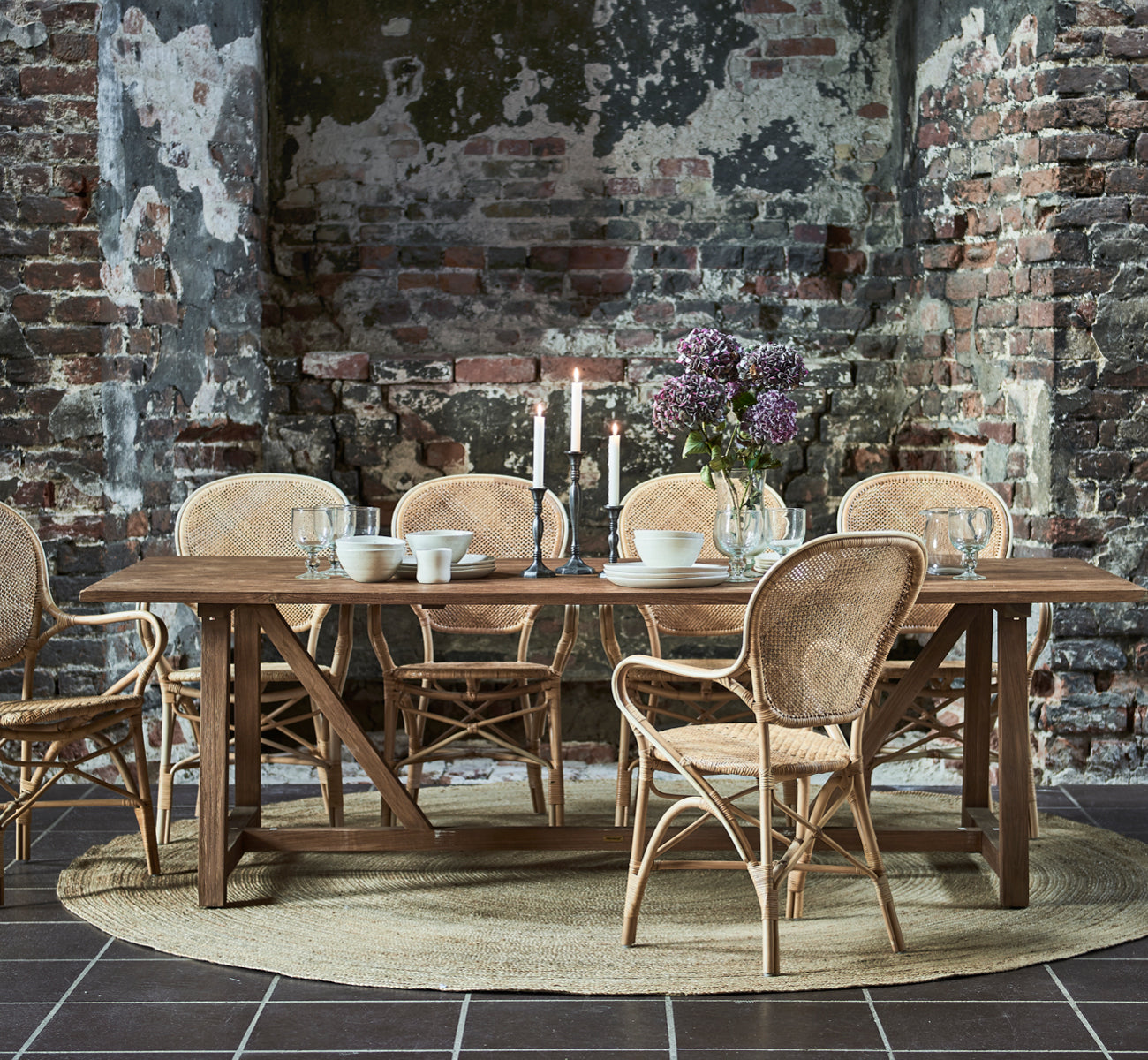 This is a lifestyle image of Rossini Dining Armchair in natural rattan. Paired with a round glass table on a jute rug in a panelled room.
