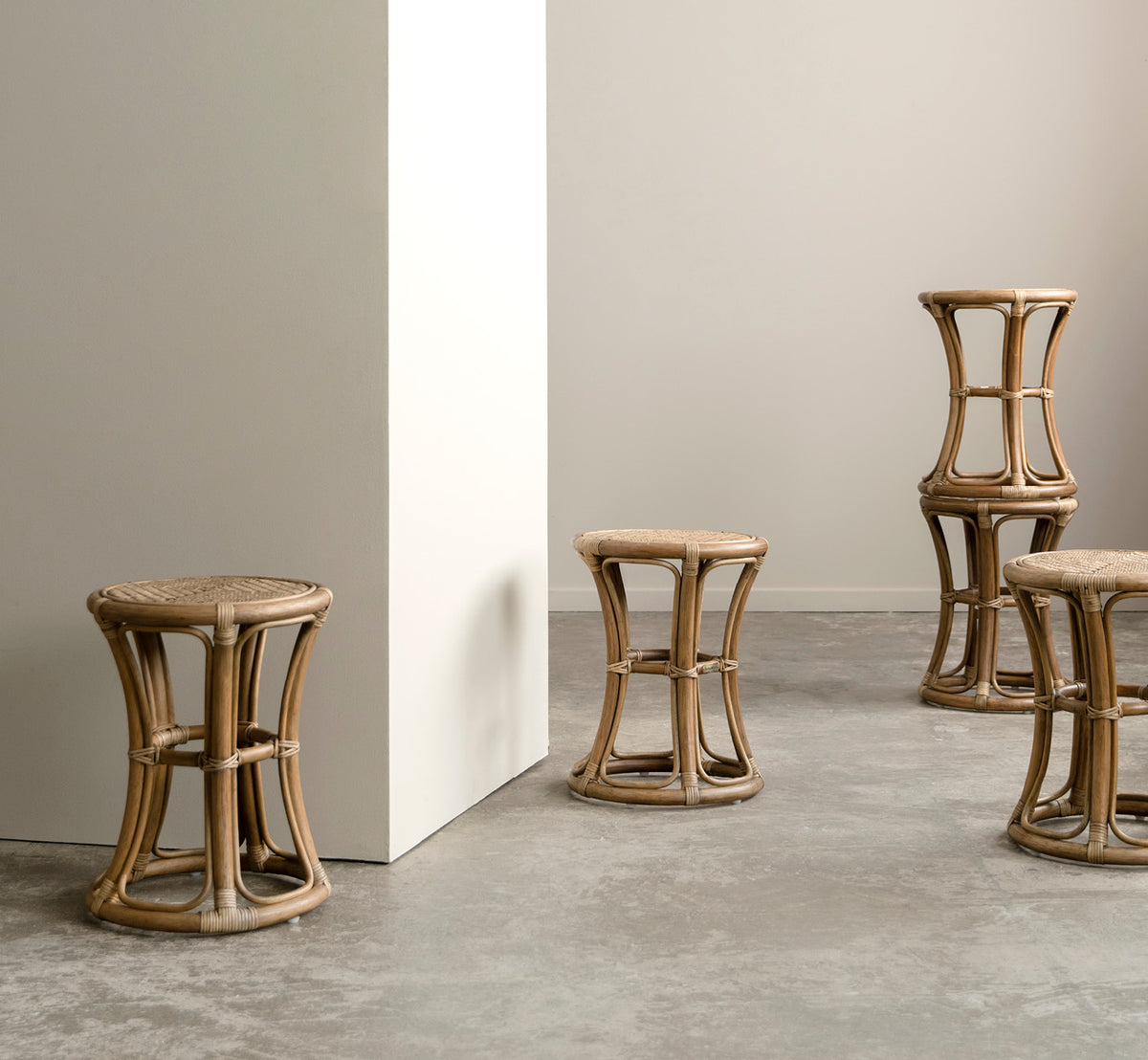 This is a lifestyle image of Bella Stool in antique rattan, in a bright interior with white panelled walls and herringbone parquet.