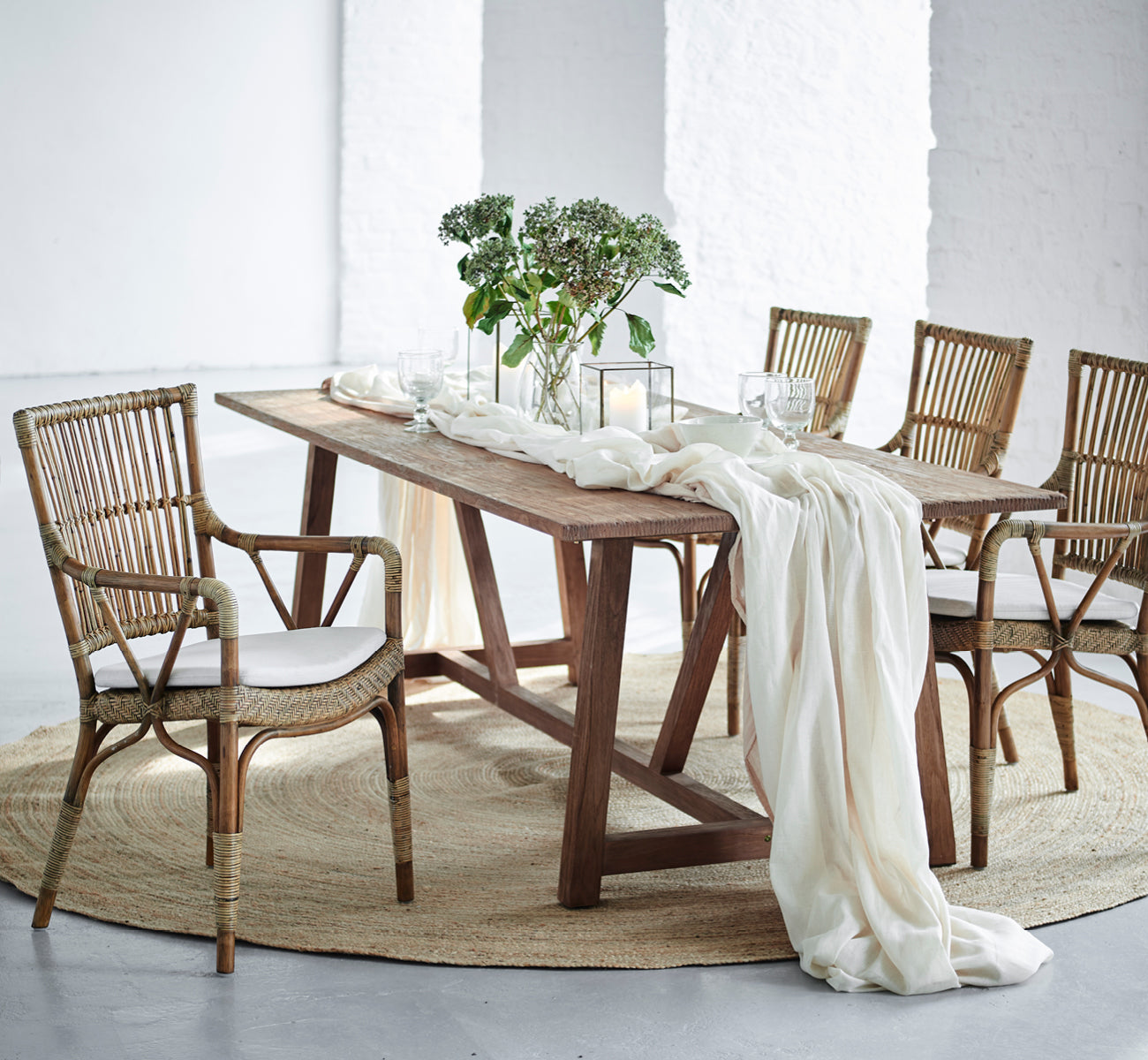 This is a lifestyle image of Piano Dining Chair in antique rattan. Around a rustic wood dining table with linen runner and candles.