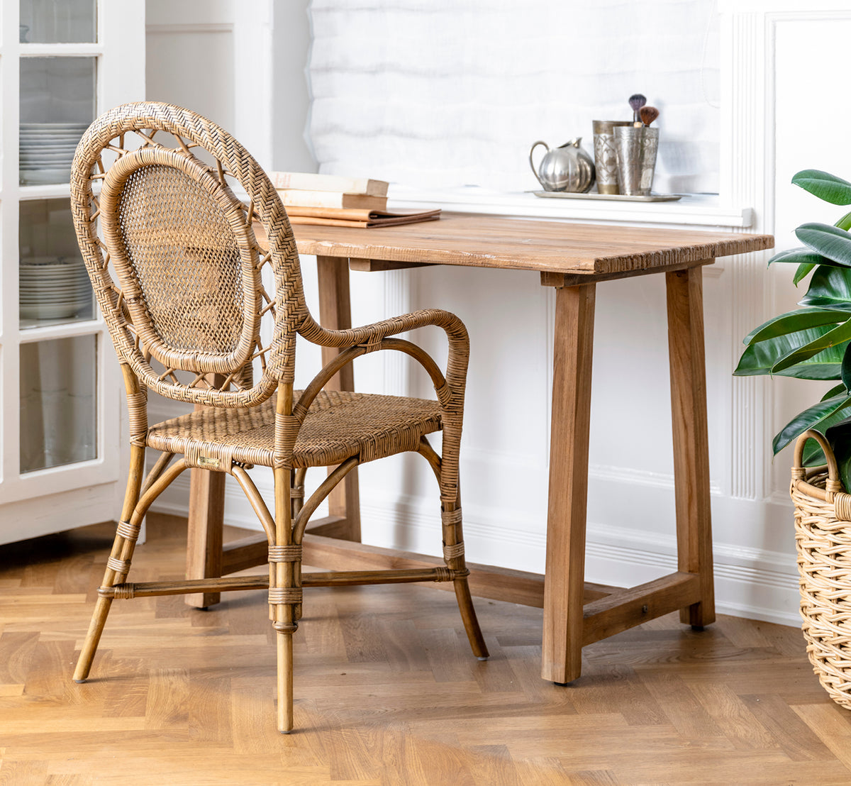 This is a lifestyle image of Romantica Dining Chair in antique rattan. Arranged in a grey stone interior niche with wrought-iron wall lamps.