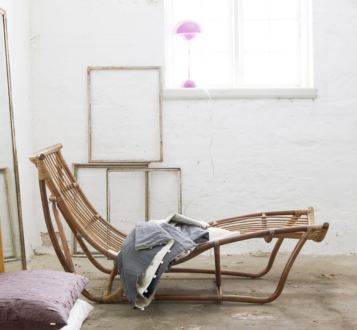 This is a lifestyle image of Michelangelo Daybed in antique rattan. Styled with linen throws in a white studio with vintage frames.