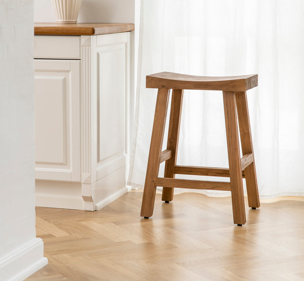 This is a lifestyle image of Charles Counter Stool in teak indoor, in a bright white interior with wainscoting and herringbone parquet.