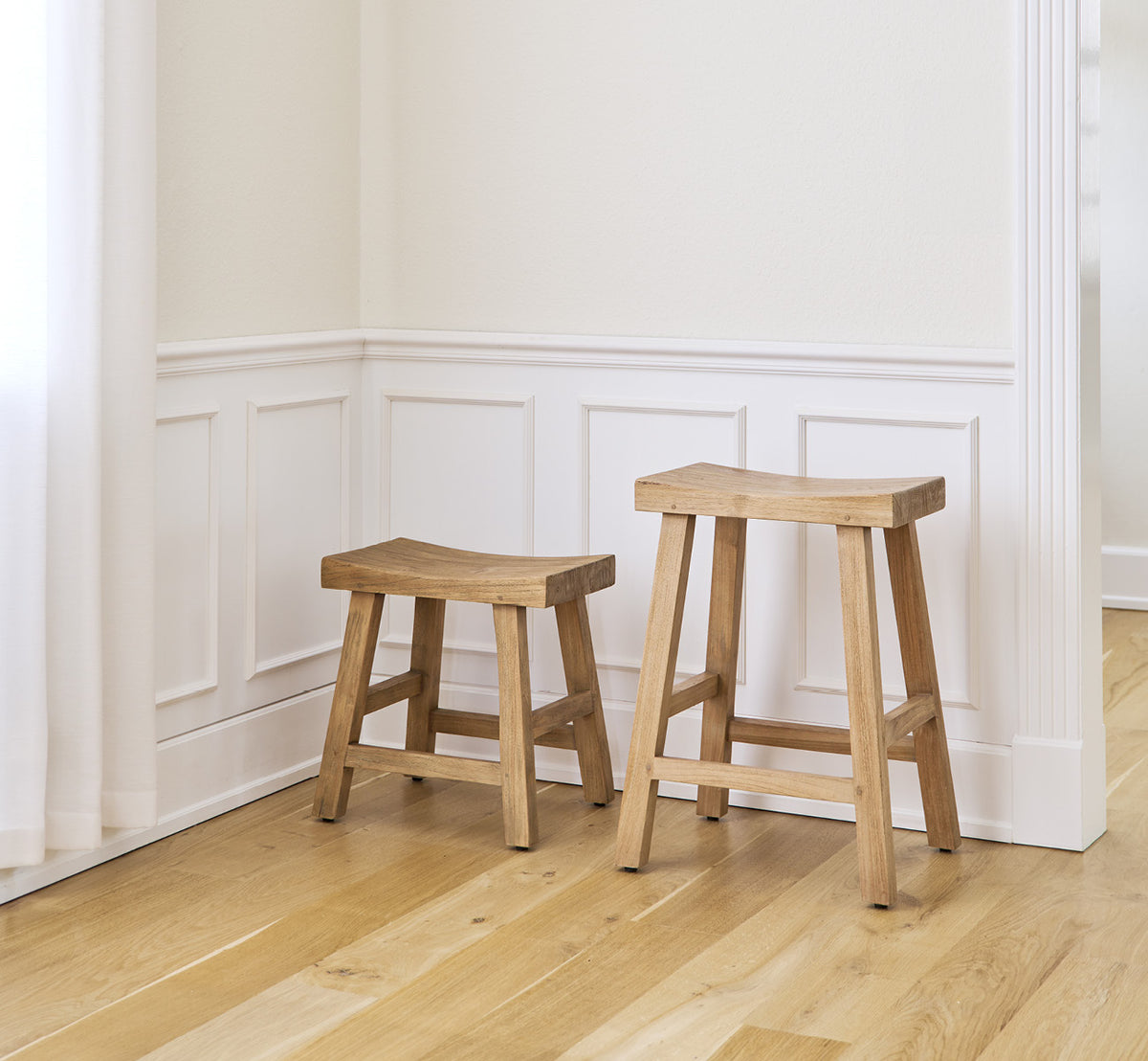 This is a lifestyle image of Charles Counter Stool in teak indoor, in a bright white interior with wainscoting and herringbone parquet.