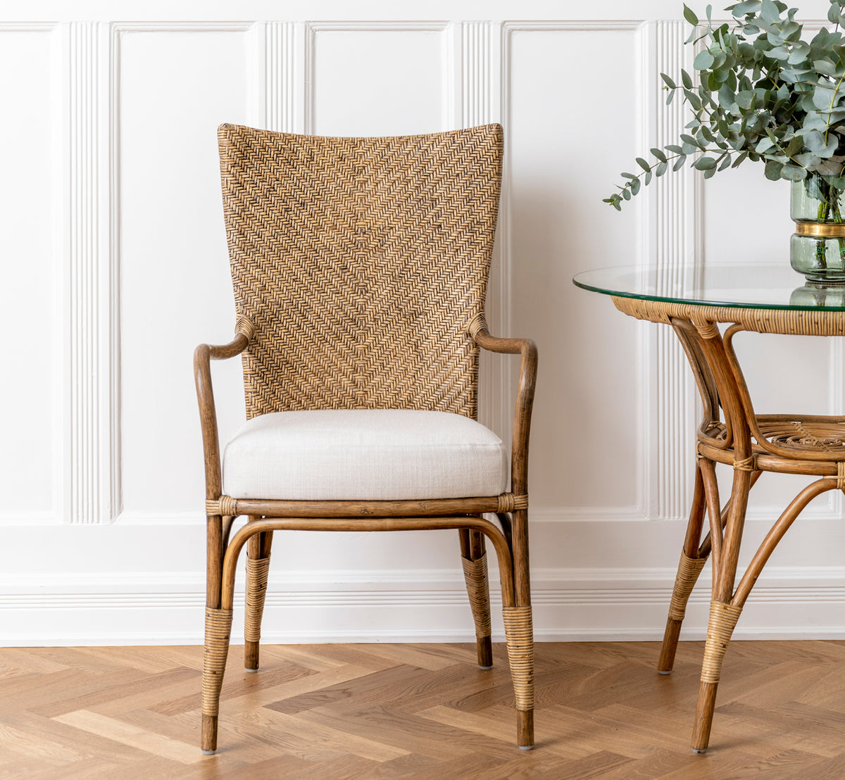 This is a lifestyle image of Melody Dining Armchair in antique rattan. Set at a white dining table in a bright Scandinavian room.