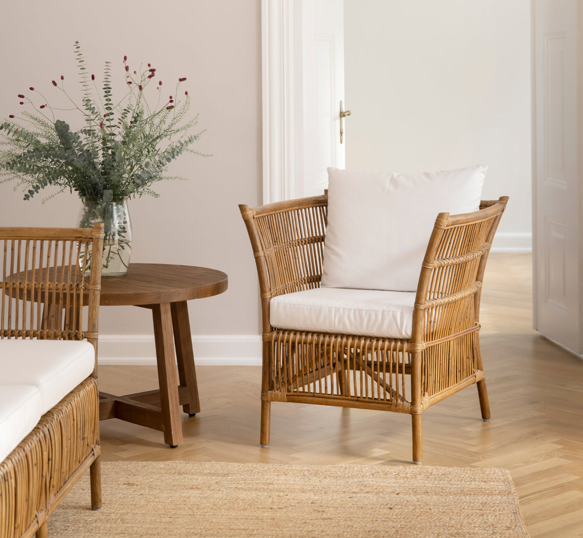 This is a lifestyle image of Donatello Lounge Chair in antique rattan, in a bright living room with herringbone parquet and lush greenery.