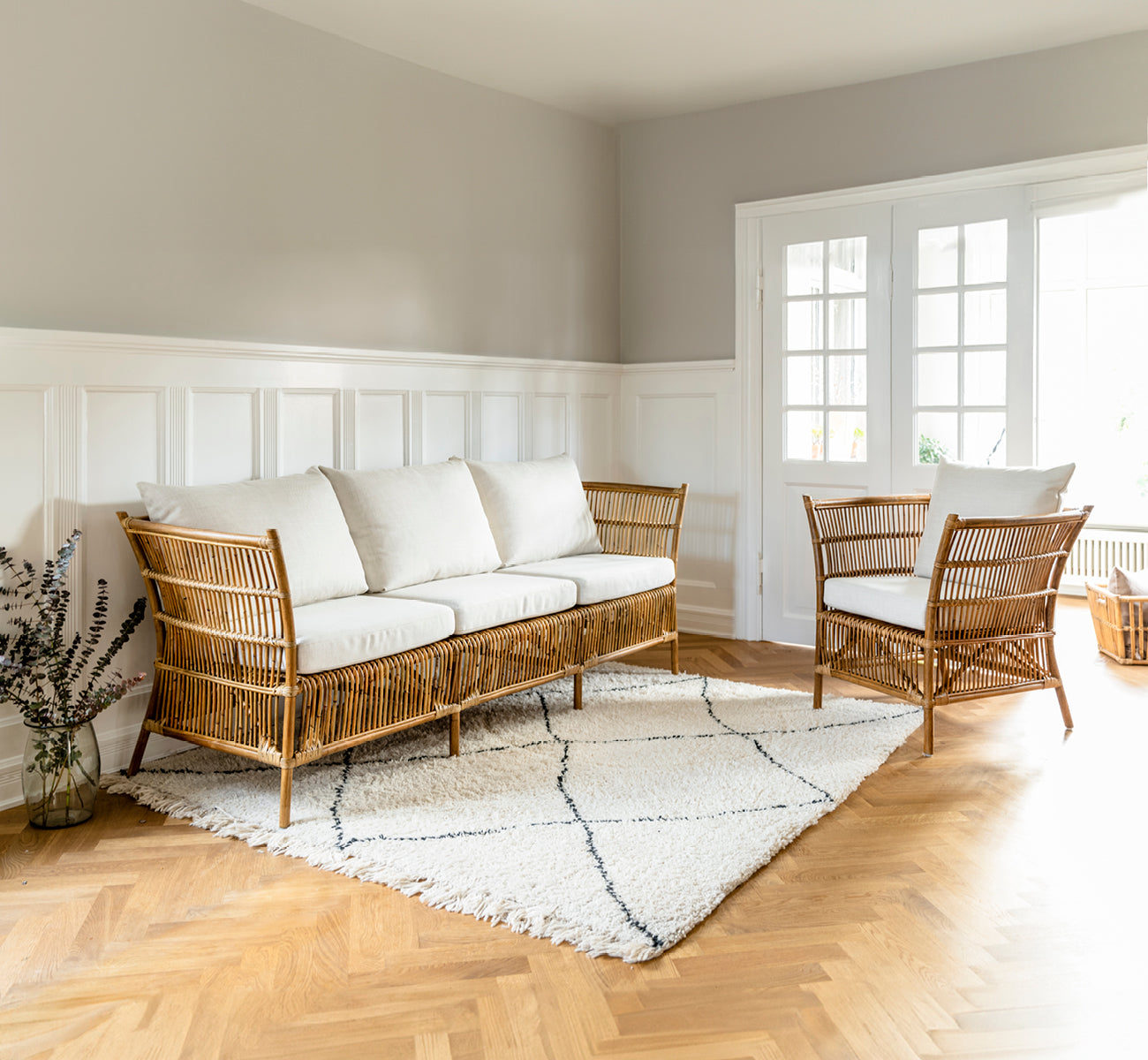 This is a lifestyle image of Donatello 3 Seater Sofa in antique rattan, in a bright interior with herringbone parquet flooring.