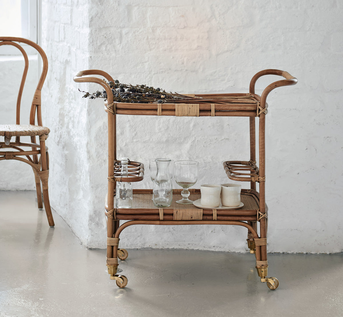 This is a lifestyle image of Carlo Trolley in antique Rattan, in a bright white interior with wainscoting and a rattan wall mirror.