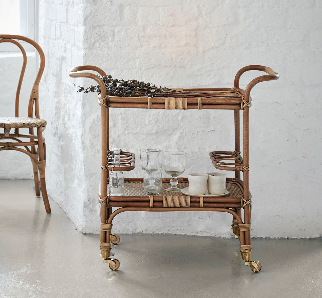 This is a lifestyle image of Carlo Trolley in antique Rattan, in a bright white interior with wainscoting and a rattan wall mirror.