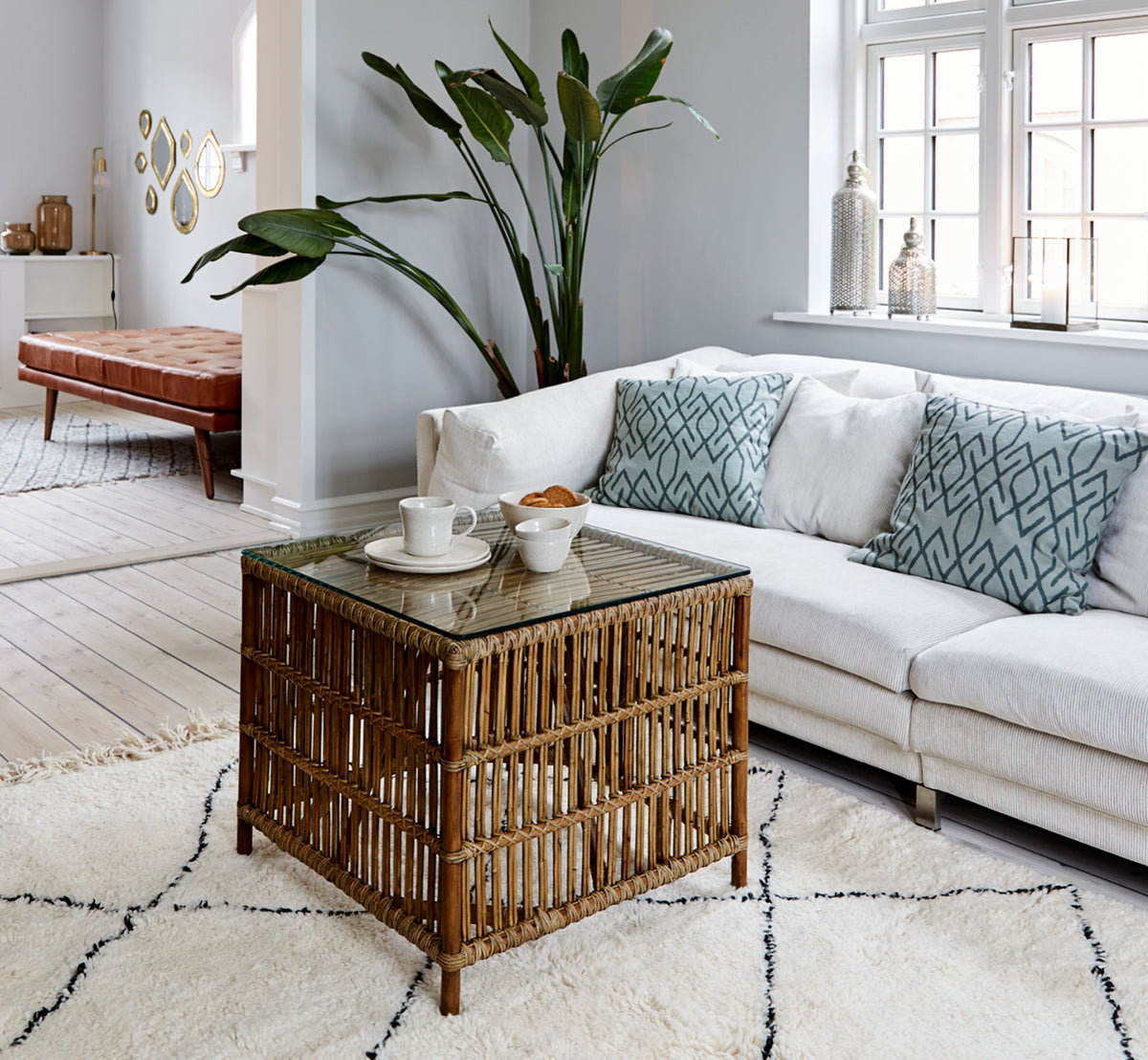This is a lifestyle image of Donatello Side Table in antique rattan, in a bright interior with white panelled walls and herringbone parquet.