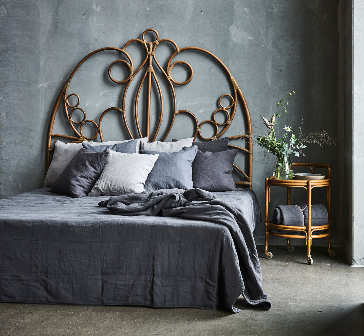 This is a lifestyle image of Natalia Headboard in antique rattan, in a serene bright bedroom with neutral linen and herringbone parquet.