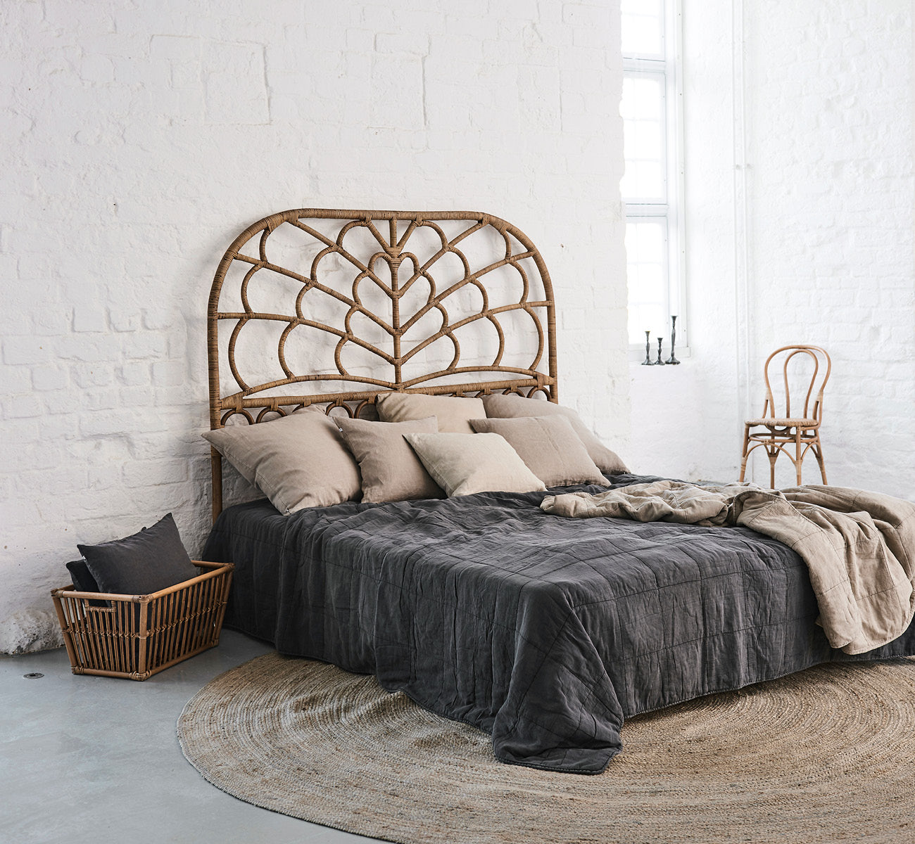 This is a lifestyle image of Celia Headboard in antique rattan, in a serene bright bedroom with neutral linen and herringbone parquet.
