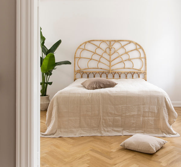 This is a lifestyle image of Celia Headboard in natural rattan, in a serene bright bedroom with neutral linen and herringbone parquet.