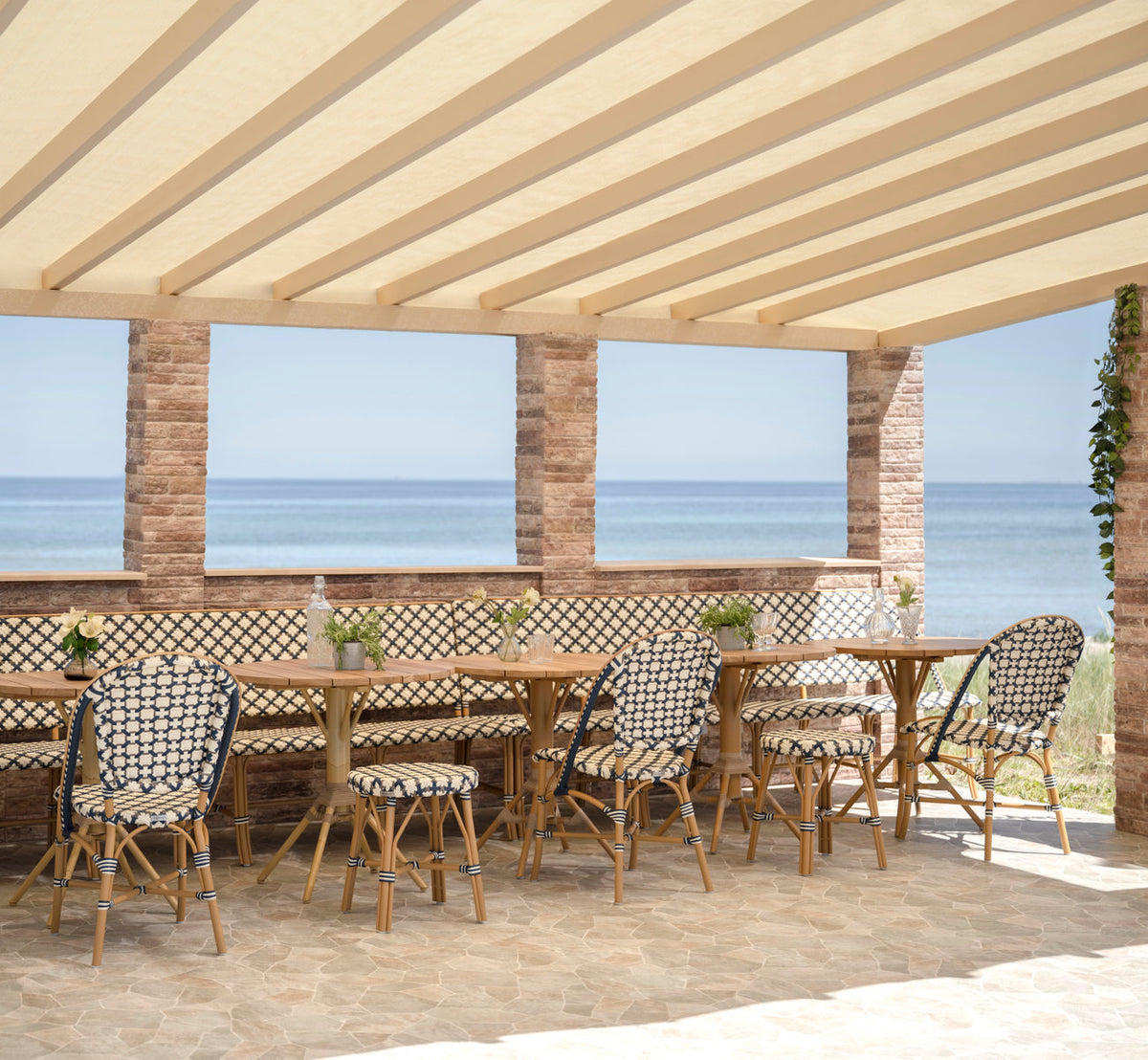 This is a lifestyle image of Sofie Exterior Dining Chair in almond aluminium frame starweave ivory navy blue cappuccino artfibre. By the sea.
