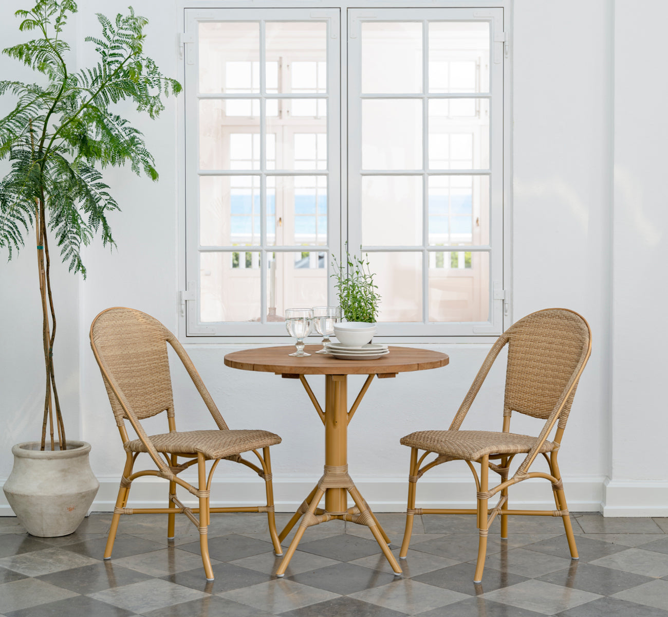 This is a lifestyle image of Sofie Exterior Dining Chair in almond aluminium frame natural ArtFibre. Around a teak outdoor table.