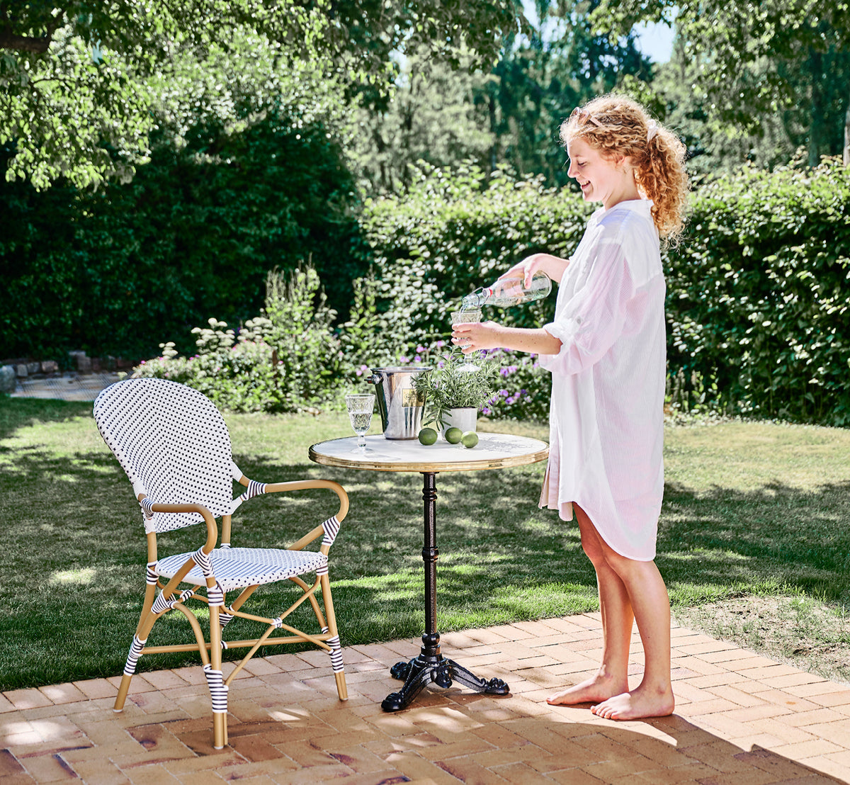 This is a lifestyle image of Isabell in almond aluminium frame White w cappuccino dot ArtFibre, in a lush garden patio with stone tile and a.