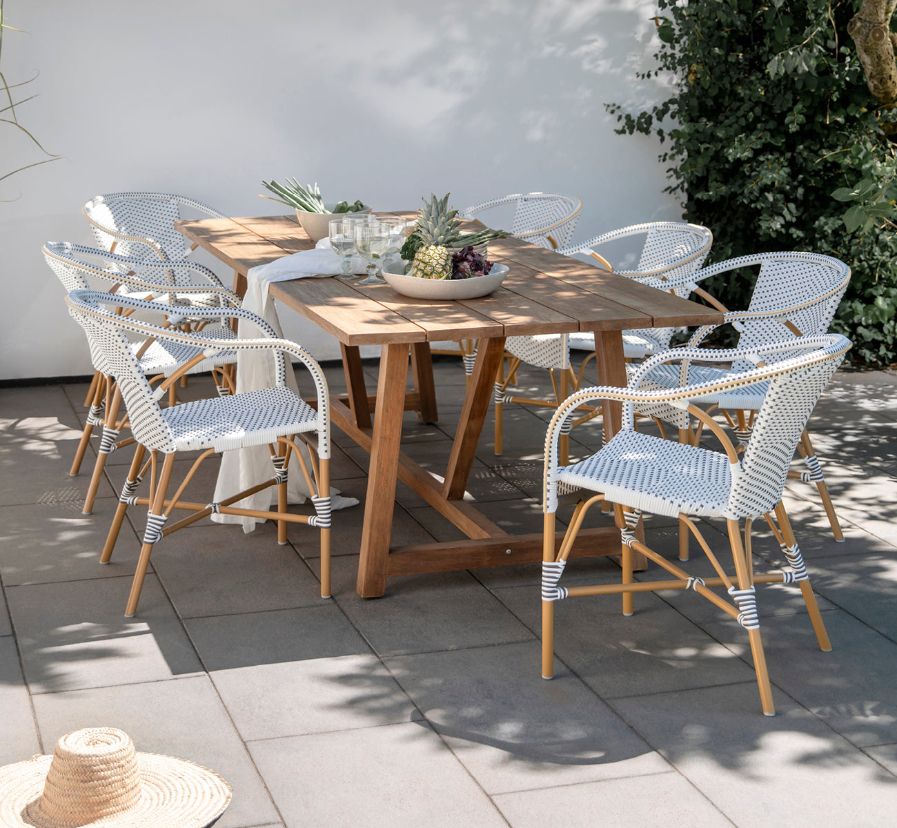 This is a lifestyle image of Madeleine Exterior Dining Chair in almond aluminium frame white w cappuccino dot ArtFibre. Garden dining with teak table.