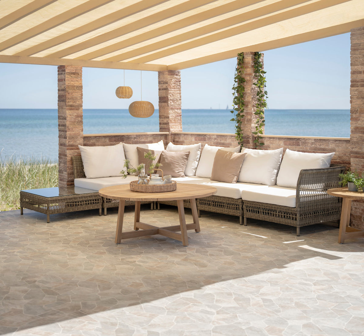 This is a lifestyle image of Mona Exterior Modular Sofa-Center Module in antique grey artfibre aluminium. Under a pergola by the sea.