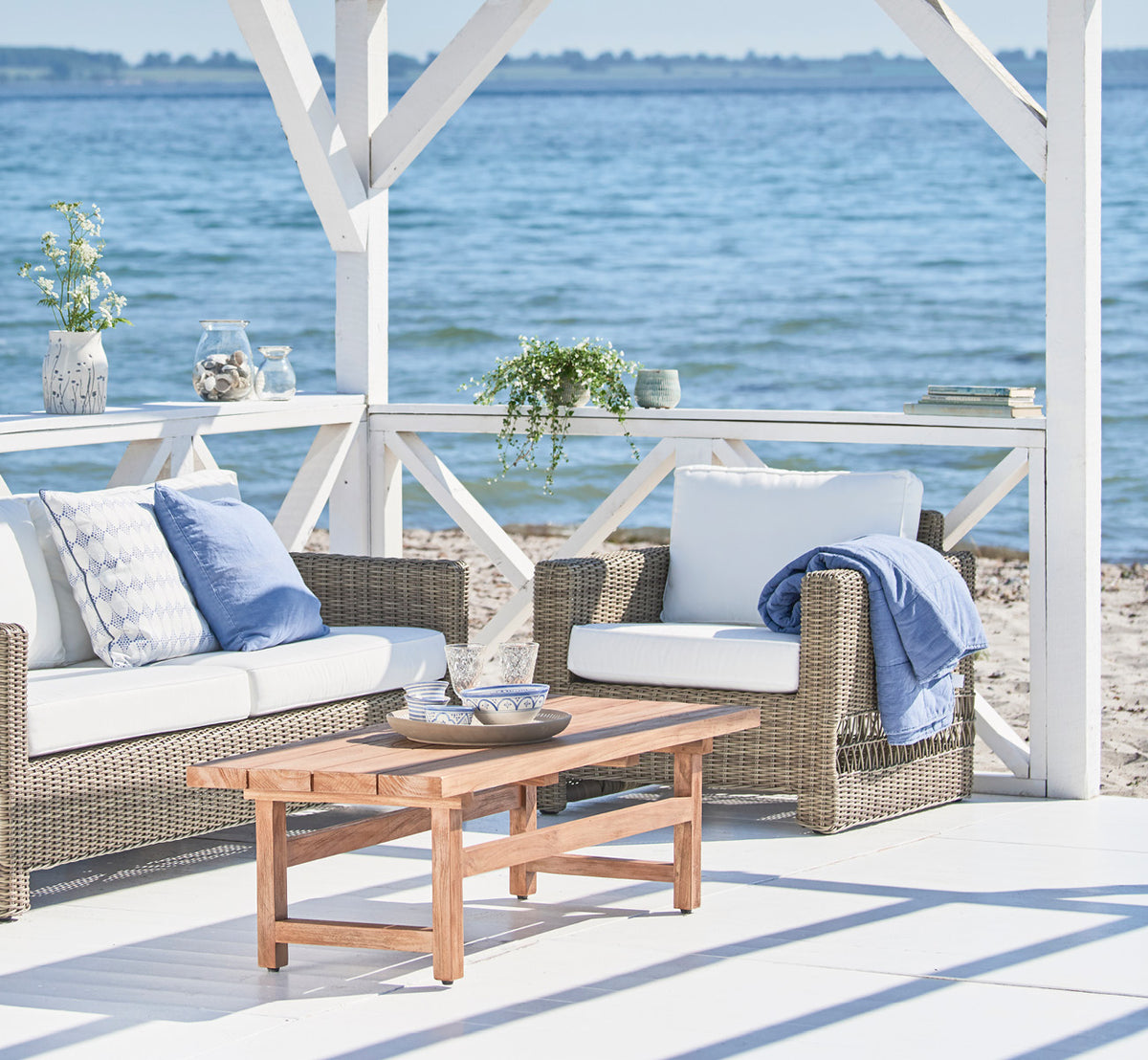 This is a lifestyle image of Carrie Lounge Chair in antique Grey ArtFibre Aluminium, on a sun-drenched coastal terrace with sea views and white.