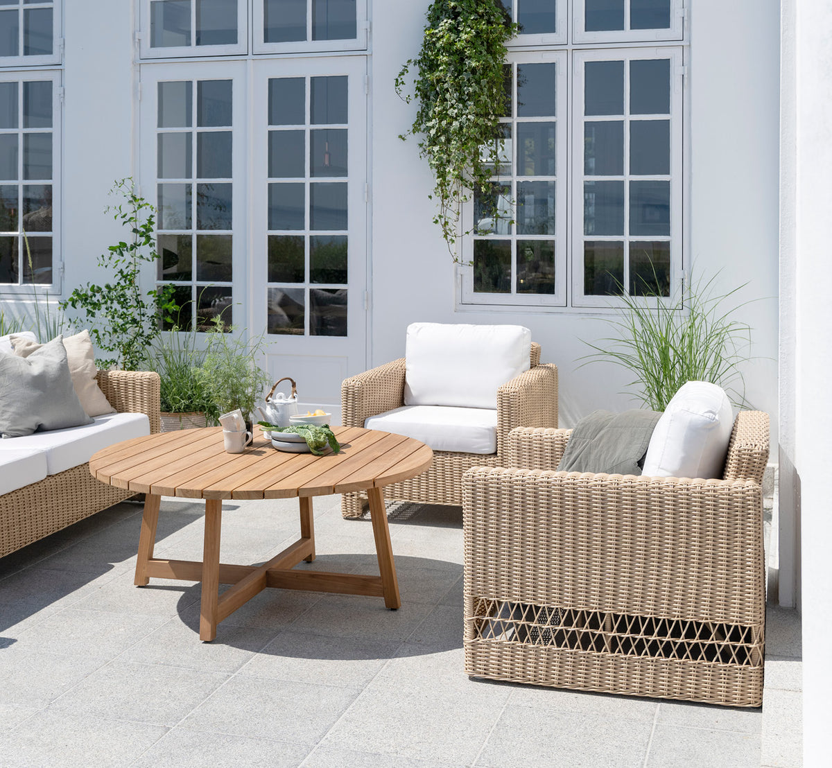 This is a lifestyle image of Carrie Lounge Chair in natural ArtFibre Aluminium, on a sun-drenched coastal terrace with sea views and white pergola.