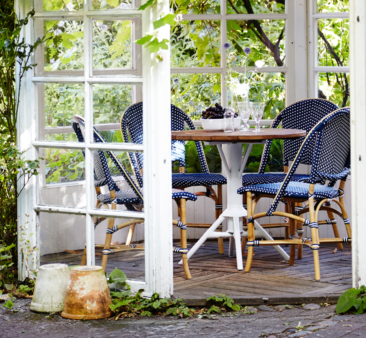 This is a lifestyle image of Sofie Dining Chair in navy blue w white dot artfibre skin on rattan frame. Styled in a bright interior setting.
