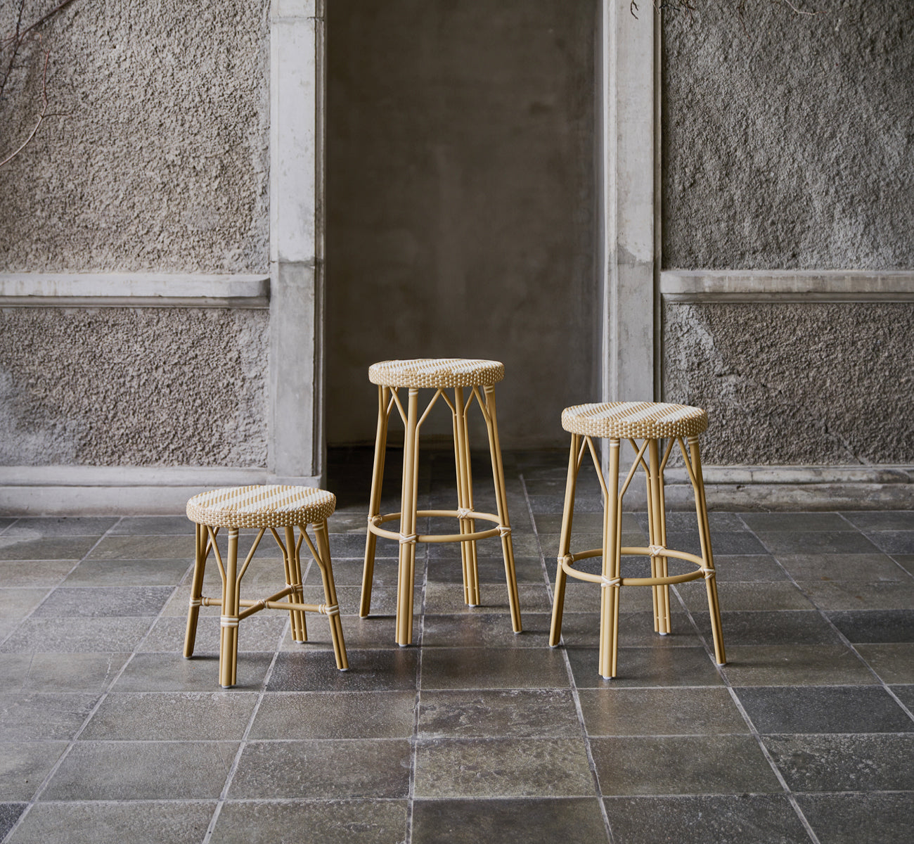 This is a lifestyle image of Simone Bar Stool in striped honey ivory ArtFibre Skin on Rattan frame. Shown in a stone courtyard.