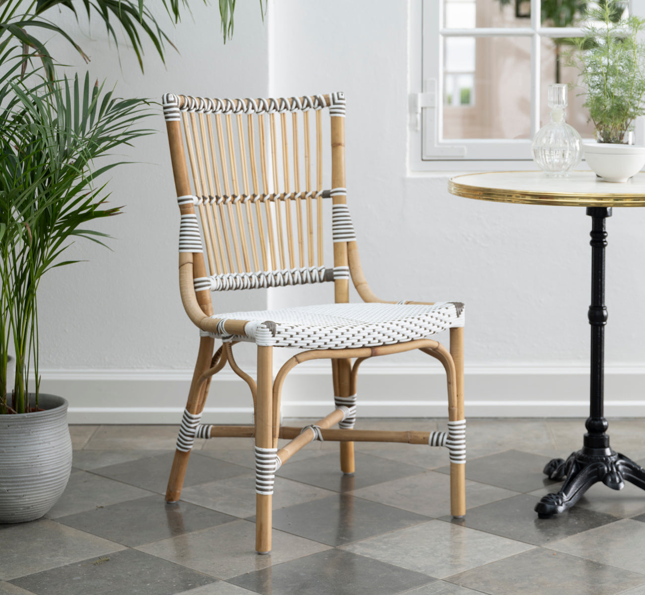 This is a lifestyle image of Monique Dining Chair in white w cappuccino dot artfibre skin on rattan frame. Styled in a bright interior setting.