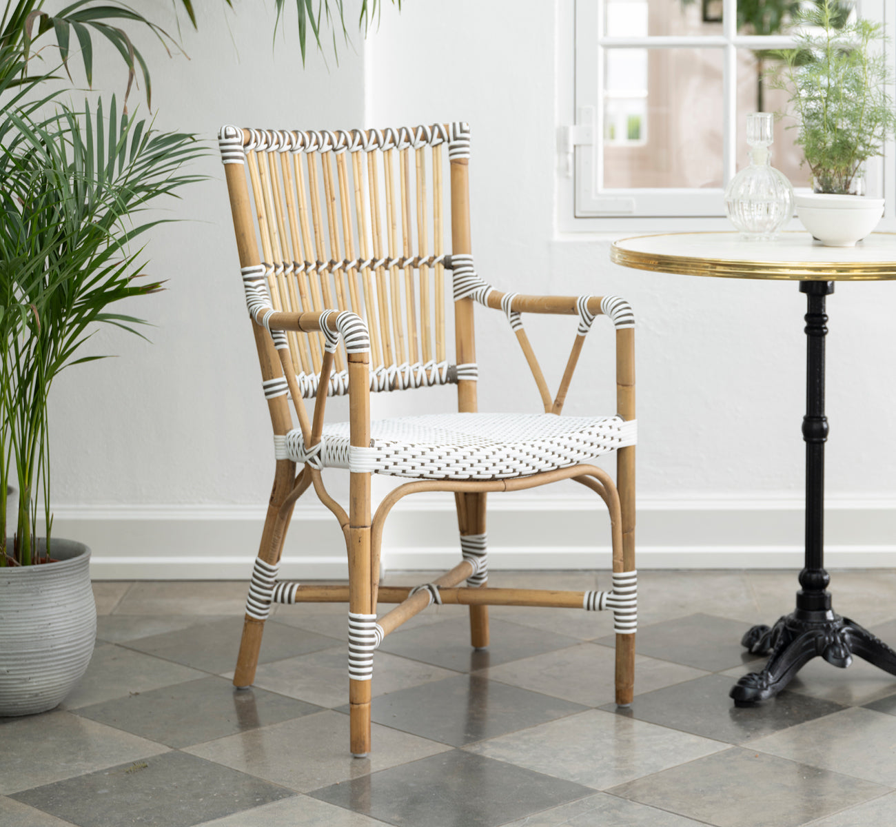 This is a lifestyle image of Monique Dining Armchair in white w cappuccino dot artfibre skin on rattan frame. Styled in a bright interior setting.