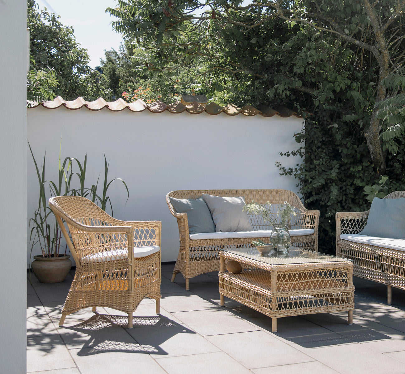 This is a lifestyle image of Charlot Chair in natural ArtFibre Aluminium, on a sun-drenched coastal terrace with sea views and a white pergola.