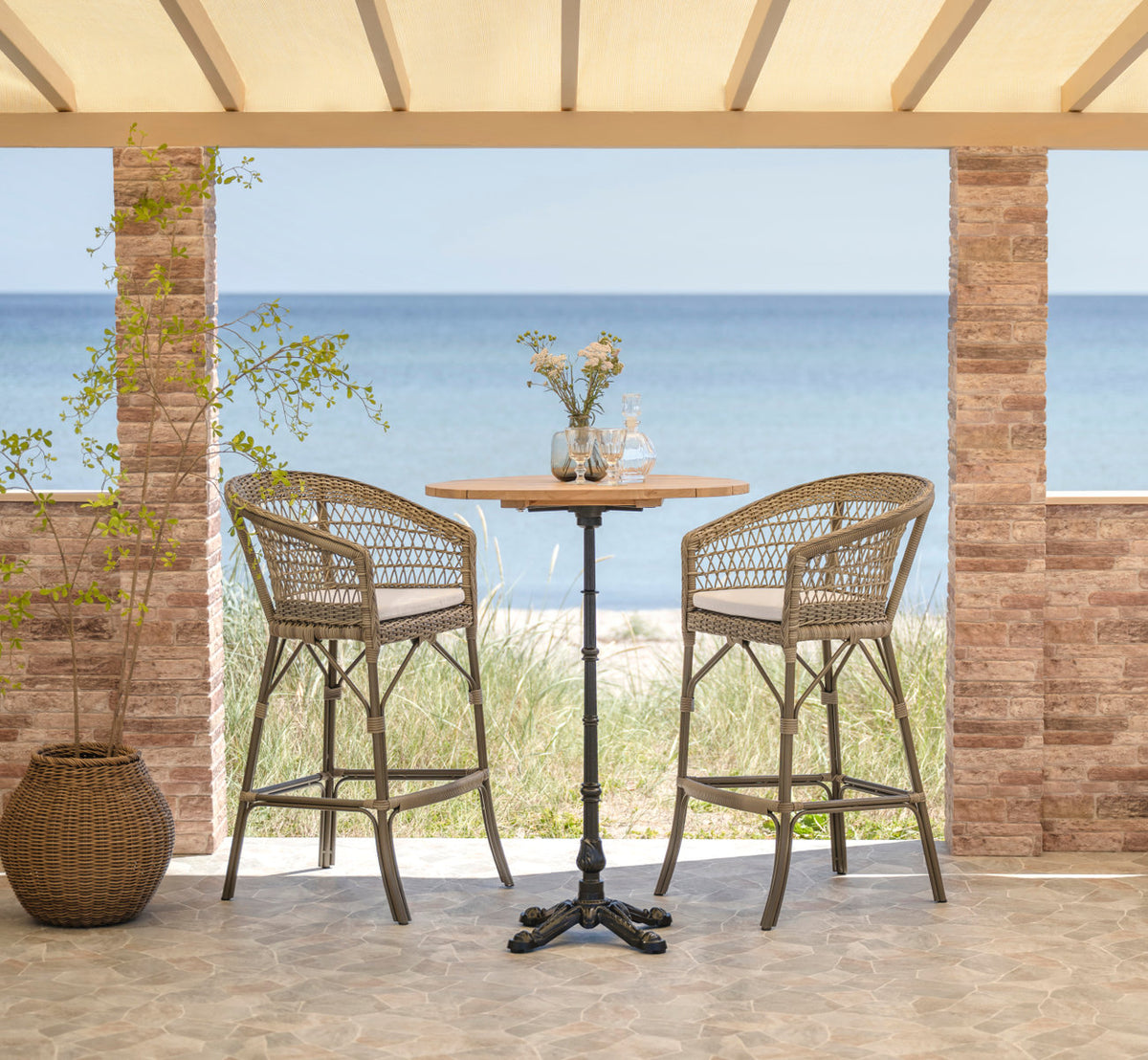This is a lifestyle image of Emma Exterior Barstool in antique grey artfibre aluminium. Bar setting with sea view.