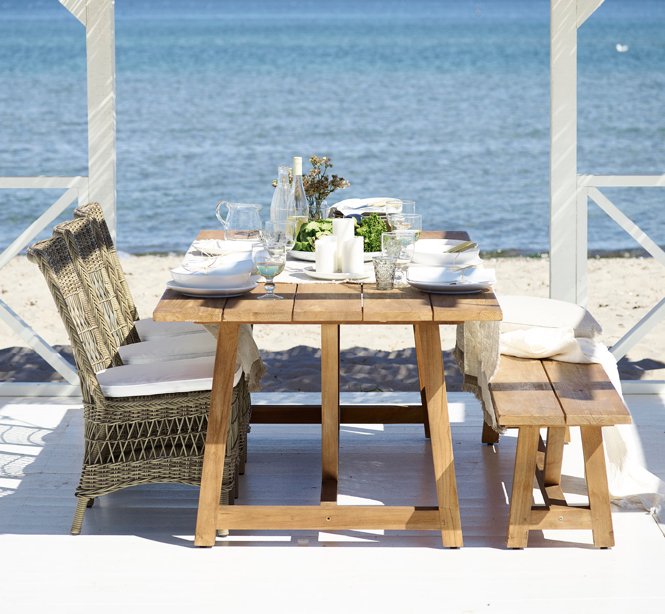 This is a lifestyle image of Marie Exterior Side Chair in antique grey artfibre aluminium. At a teak table on a seaside pavilion.