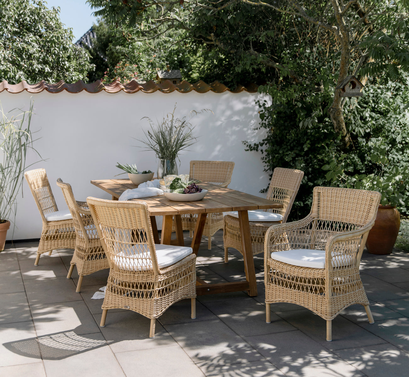 This is a lifestyle image of Marie Exterior Armchair in natural artfibre aluminium. Styled in a bright interior setting.