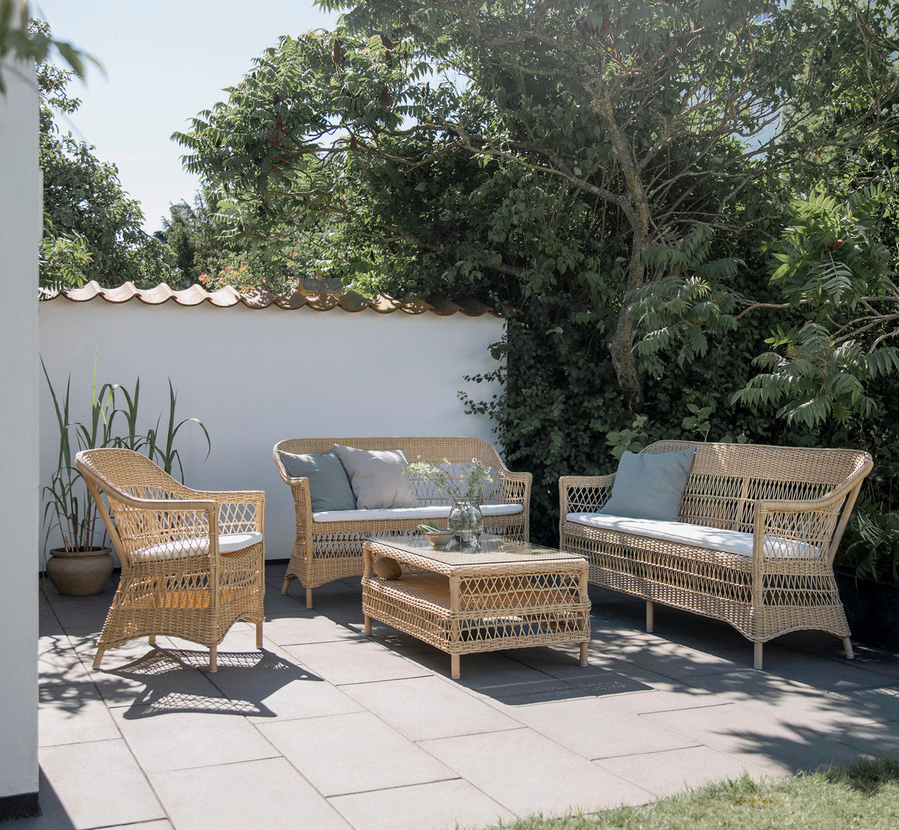 This is a lifestyle image of Charlot 2 Seater Sofa in natural ArtFibre Aluminium, on a coastal terrace with reed roof, sea views and striped cushions.