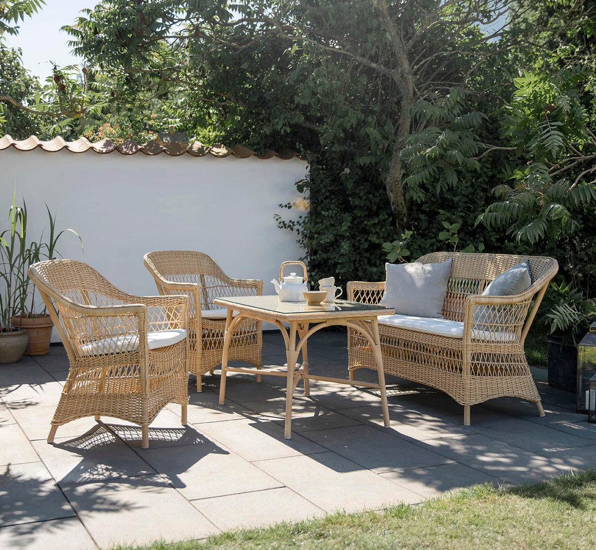 This is a lifestyle image of Charlot 2 Seater Sofa in natural ArtFibre Aluminium, on a coastal terrace with reed roof, sea views and striped cushions.
